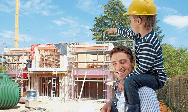 Vater mit Sohn auf den Schultern vor einer Baustelle