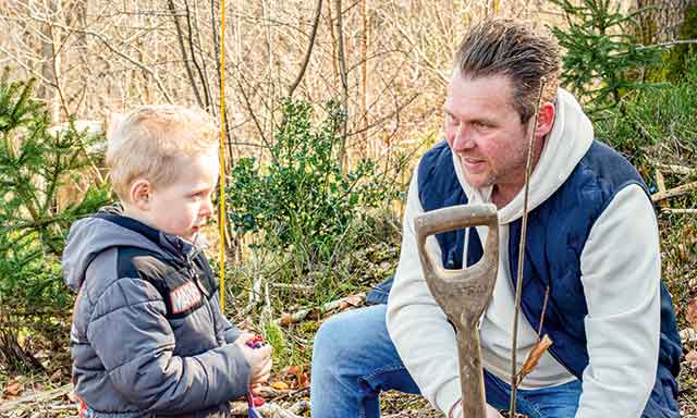 Mann mit einem Kleinkind kniet auf dem Waldboden