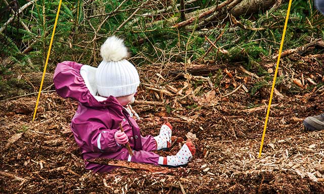 Kleines Kind sitzt auf einem Waldboden