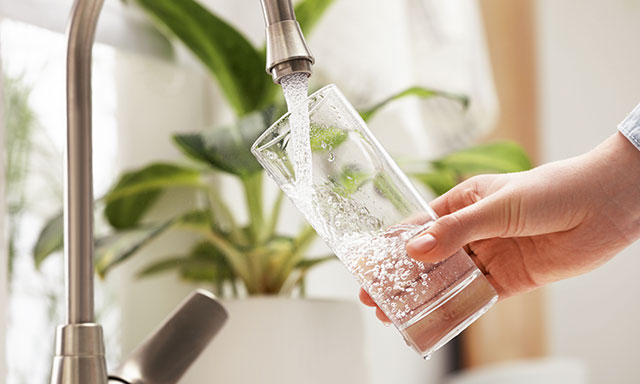 Hand hält ein Glas unter einen Wasserhahn