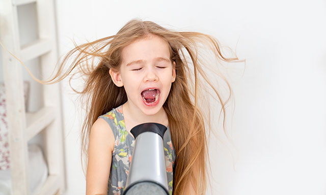 Kind bläst sich mit einem Föhn Wind ins Gesicht